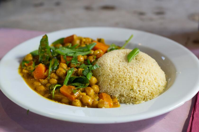 Chickpeas in orange sauce with carrots and green leaves with a side of quinoa on a white plate.
