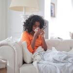 Woman blowing her nose while sitting on a couch.