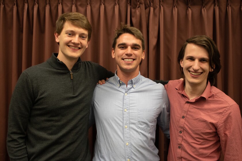 Three microbiology and molecular biology students stand smiling in front of a red curtain.