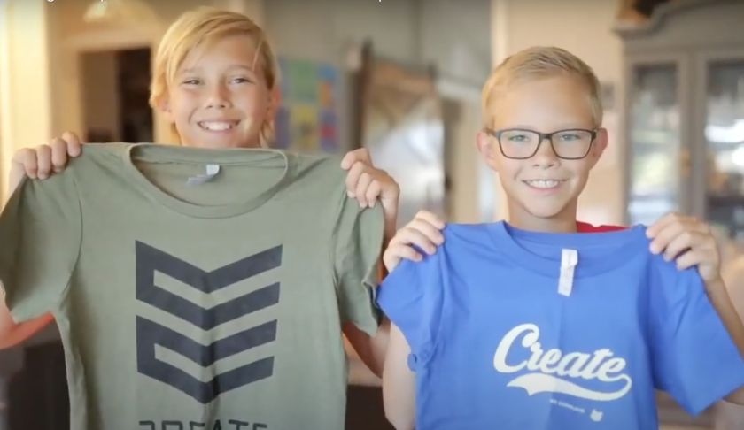 Two boys, Tanner and Tate Smith, smile while holding up a green and a blue T-shirt with a black design and the word "create" on them.