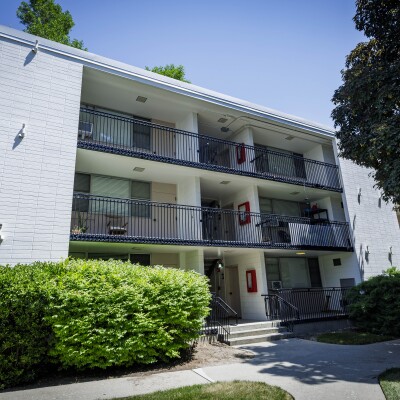 Exterior of a Wymount Terrace apartment building with shaded walkways, balconies, and surrounding trees and bushes.