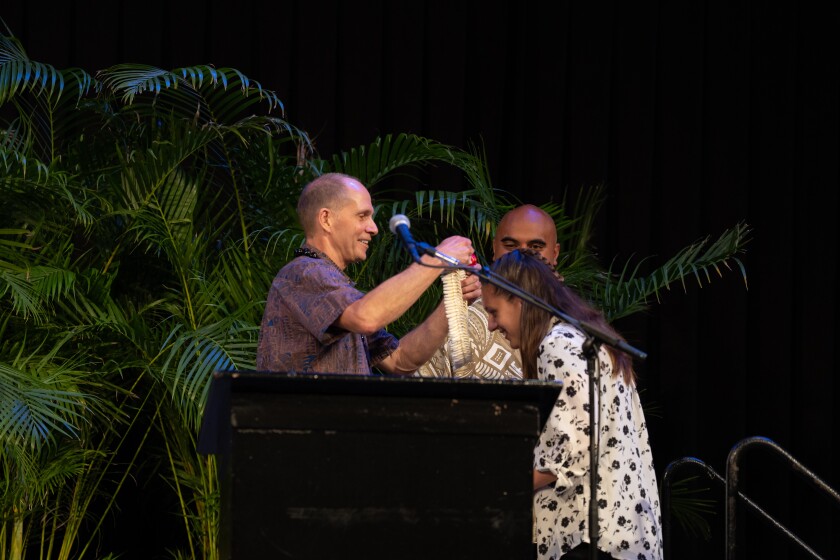 A woman bends to receive a lei from a man at a podium.