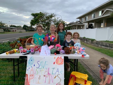 A table set up on Kulanui Street in Laie has toys for sale by 6 kids with a sign that reads "Save Australia + Philippines