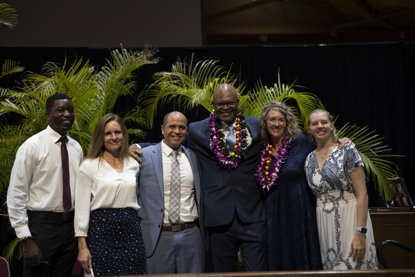 landscape shot of devotional speaker, his wife, the two students who gave the prayers, and President and Sister Kauwe smiling for a group photo in front of greenery in the Cannon Activities Center