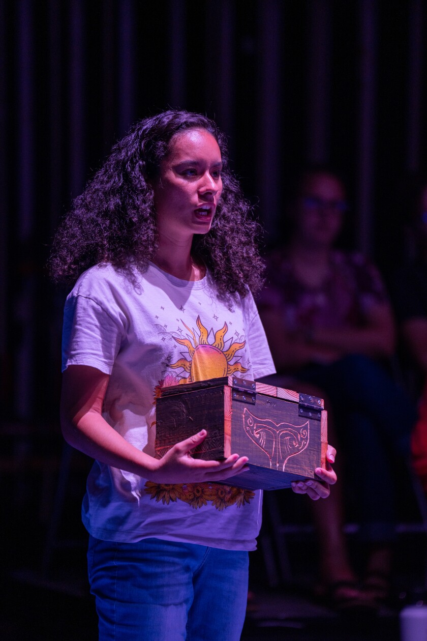 Woman holding a box onstage while performing.