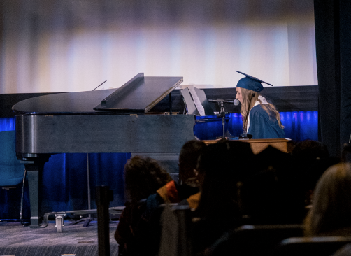 A young woman plays the piano and sings into a microphone