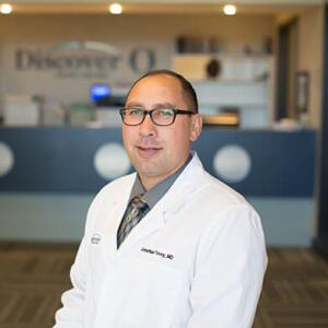 Jonathan Tovey smiling at the camera wearing a white coat.