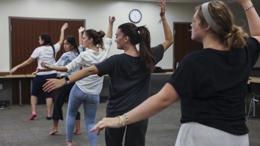 Female students dancing in a line with arms raised.