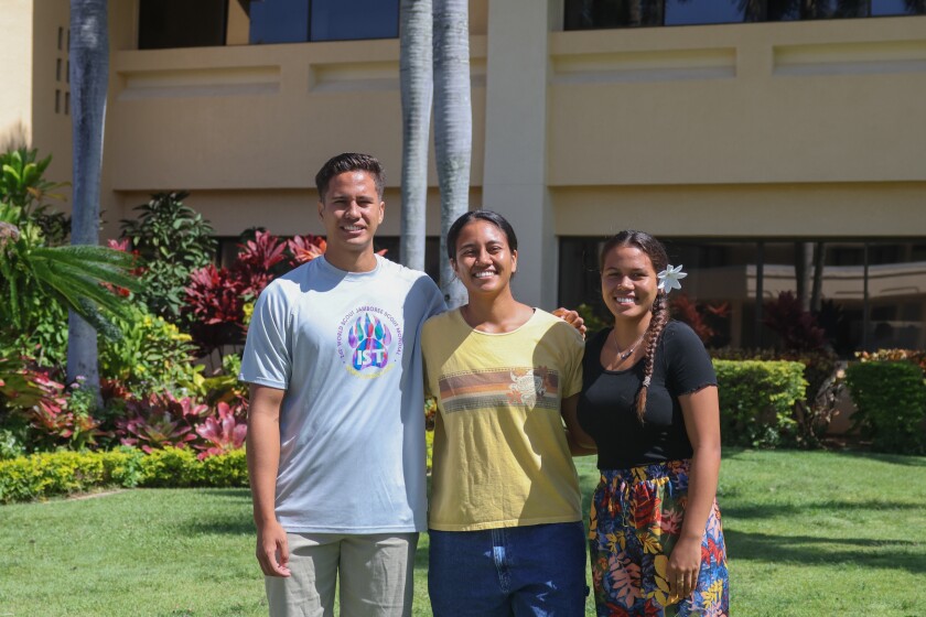 A man and two women smile and pose outside.