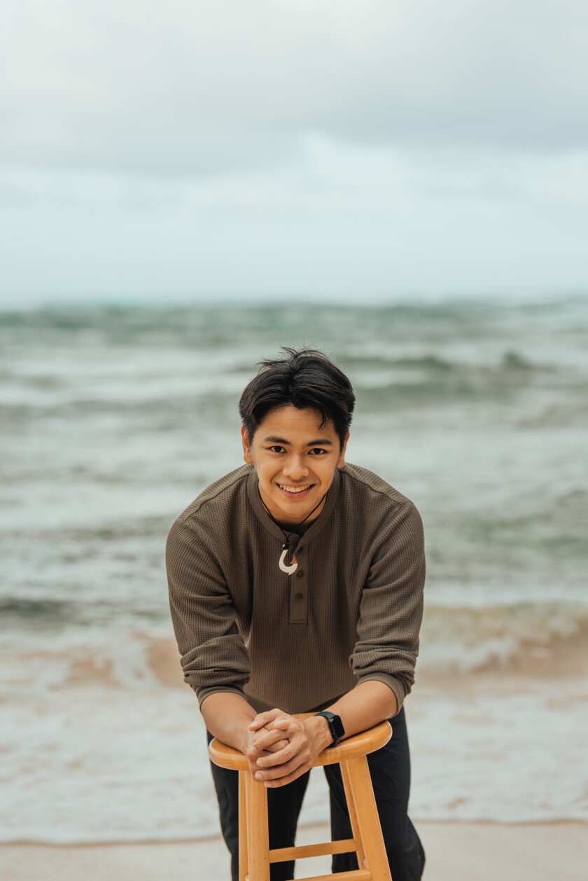 Alden Kiel stands and leans forward on a wooden stool, smiling slight as he faces the camera.