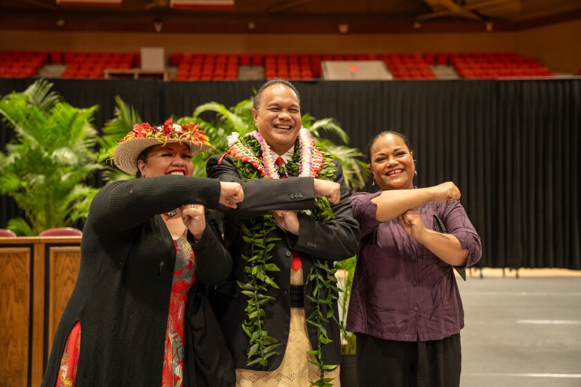A an and two women stand smiling at the camera and making a "T" with their arms.