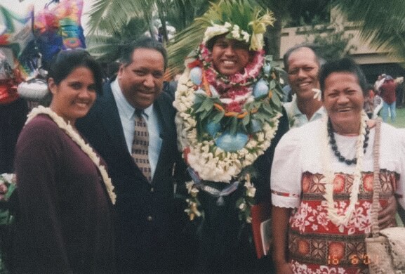 A vintage of two women and two men stand with a graduate who is wearing a ton of leis.