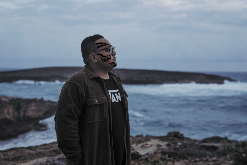A man standing on a huge rock at Laie point looking away from the camera.