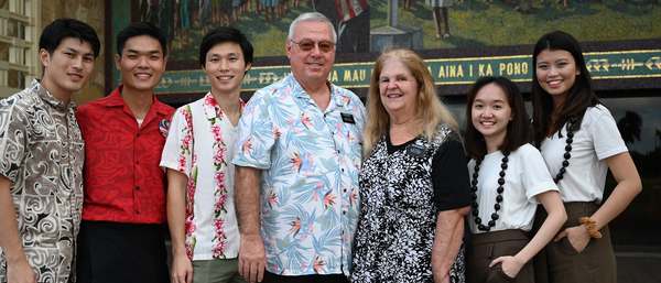 Five students with Elder and Sister McCarty standing outside in front of a campus mural.