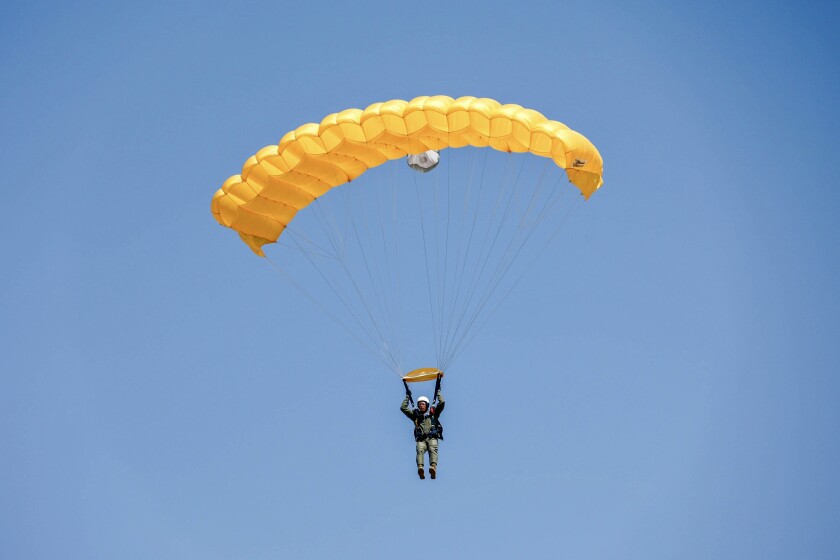 Parker hangs in a clear blue sky from a yellow parachute.