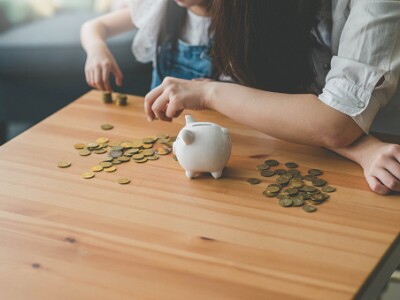 child and adult putting money in a piggy bank