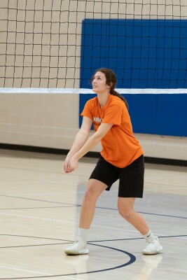 Corinne Vorkink stands in bumping volleyball stance wearing an orange shirt and black shorts.
