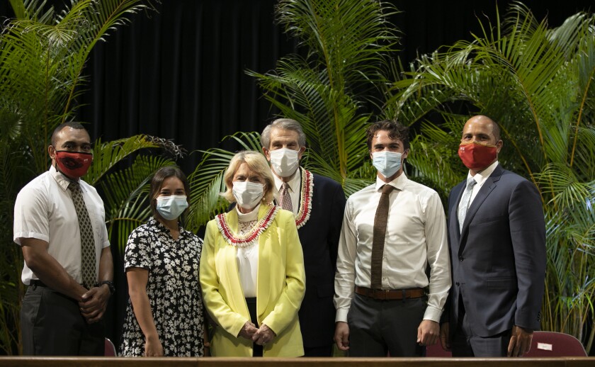 President Hallstrom standing with his wife in front of him, three students on their sides and President Kauwe on the far right, all wearing masks and formal attire with palm trees behind them.