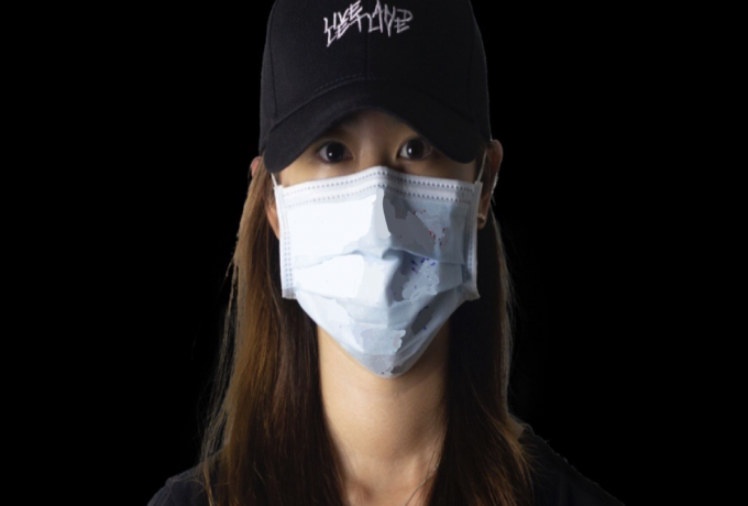 A student looks into the camera wearing a black hat and a mouth mask