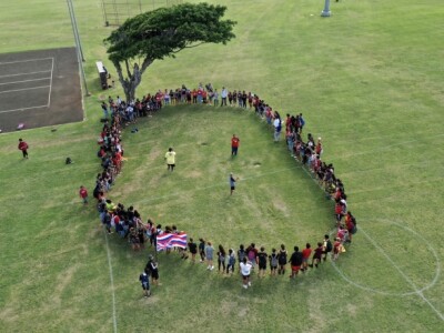 Local opponents of the wind turbine gather in a circle with the Hawaiian flag