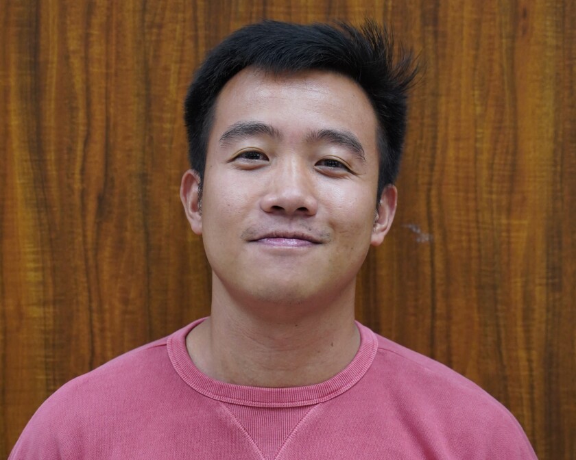 portrait of male student standing against wood background wearing plain pink sweatshirt